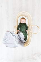 Load image into Gallery viewer, a baby boy in a bassinet wearing our moss green knotted gown with our heathered grey swaddle draped over the bottom of the bassinet