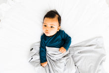 Load image into Gallery viewer, baby boy wearing our knotted baby gown in midnight teal and covered in our heathered grey stretch swaddle blanket