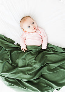 a baby girl wearing our light pink knotted gown while covered with our moss green swaddle blanket