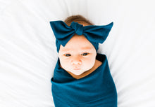 Load image into Gallery viewer, baby girl wrapped in our bamboo stretch swaddle blanket and wearing our headband in midnight teal