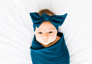 baby girl wrapped in our bamboo stretch swaddle blanket and wearing our headband in midnight teal