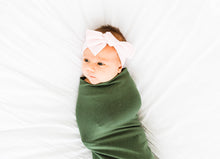 Load image into Gallery viewer, a baby girl wrapped in our moss green bamboo swaddle blanket and wearing our light pink bamboo stretch headband