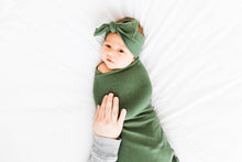 Load image into Gallery viewer, a baby girl wrapped in our moss green bamboo swaddle blanket while also wearing our bamboo stretch headband in moss green