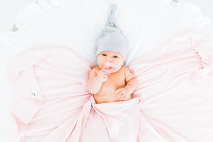 a baby girl wrapped in our bamboo stretch swaddle blanket while wearing our top knot hat in heathered grey