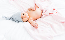 Load image into Gallery viewer, a baby girl wearing our heathered grey top knot hat and wrapped in our light pink swaddle blanket