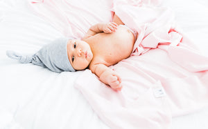 a baby girl wearing our heathered grey top knot hat and wrapped in our light pink swaddle blanket