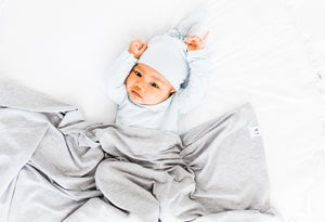 a baby boy wearing our baby blue stripe knotted gown and top knot hat while covered in our swaddle blanket in heathered grey