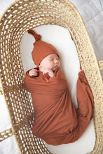 Load image into Gallery viewer, Baby wrapped in our Rust coloured swaddle and wearing matching top knot hat in rust