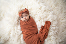 Load image into Gallery viewer, baby girl wrapped in our rust coloured swaddle blanket with matching headband
